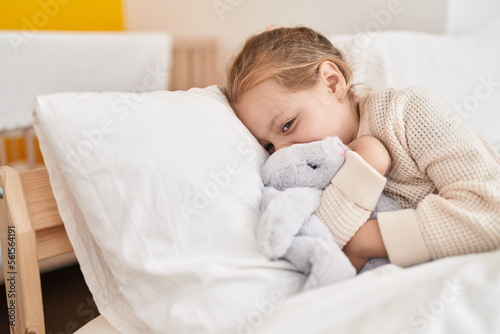 Adorable blonde girl hugging rabbit doll lying on bed at bedroom