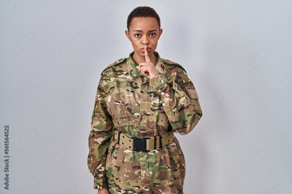 Beautiful african american woman wearing camouflage army uniform asking to be quiet with finger on lips. silence and secret concept.