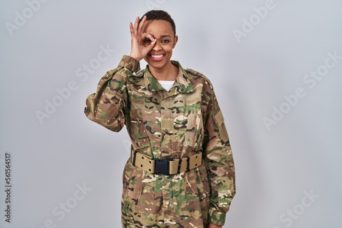 Beautiful african american woman wearing camouflage army uniform doing ok gesture with hand smiling, eye looking through fingers with happy face.