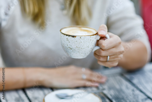 Closeup of hands of woman drinking cappuccino and cup of coffee while waiting for friend and breakfast. Happy alone woman in outdoor cafe or restaurant on sunny summer day.