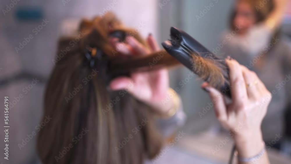 Woman fixing her hair in front of the mirror, using a hair straightener. Woman fixing her hair in front of the mirror, using a hair straightener.