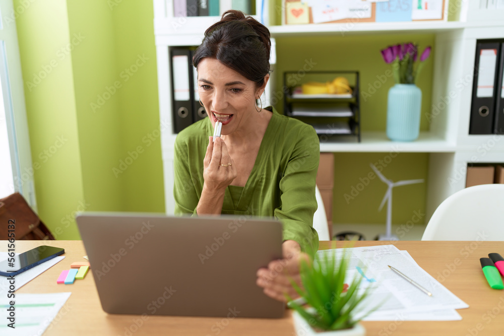 Middle age hispanic woman business worker using laptop as a mirror make up lips at street Middle age hispanic woman business worker using laptop as a mirror make up lips at street