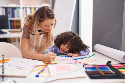 Teacher and toddler sitting on table drawing on paper at kindergarten
