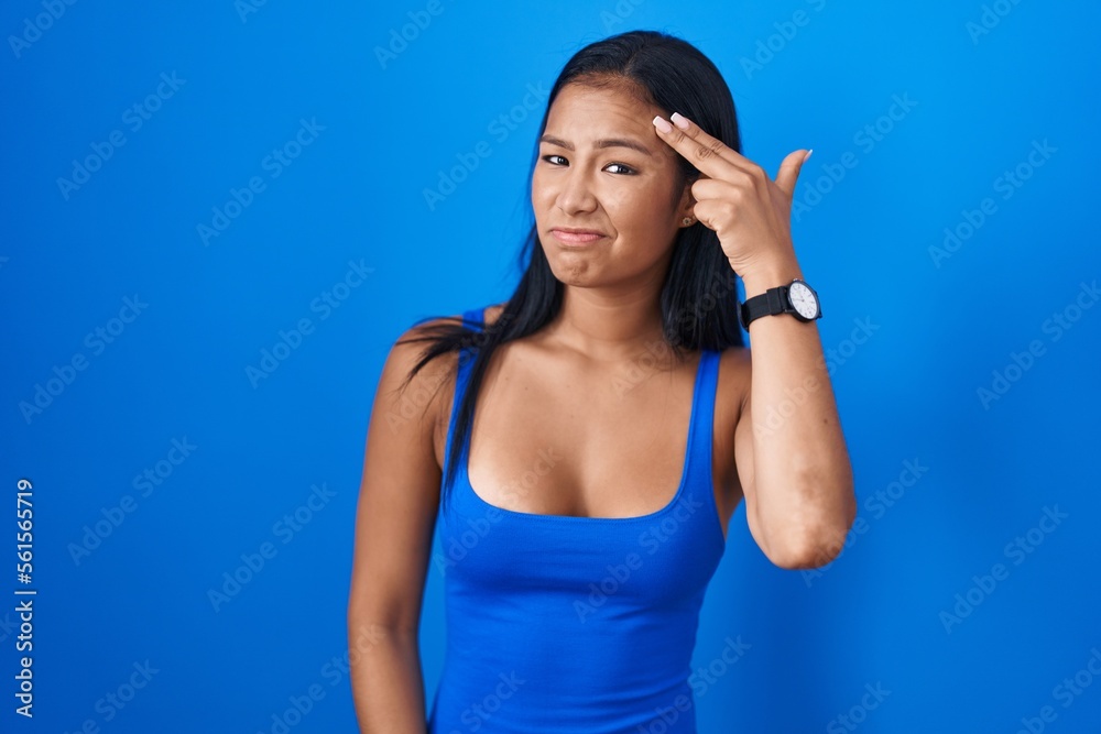 Hispanic woman standing over blue background shooting and killing oneself pointing hand and fingers to head like gun, suicide gesture. Hispanic woman standing over blue background shooting and killing oneself pointing hand and fingers to head like gun, suicide gesture.