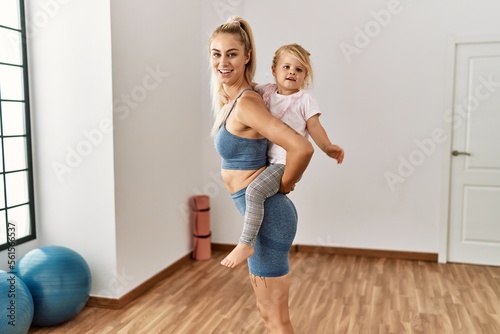 Mother and daughter smiling confident holding child on back at sport center