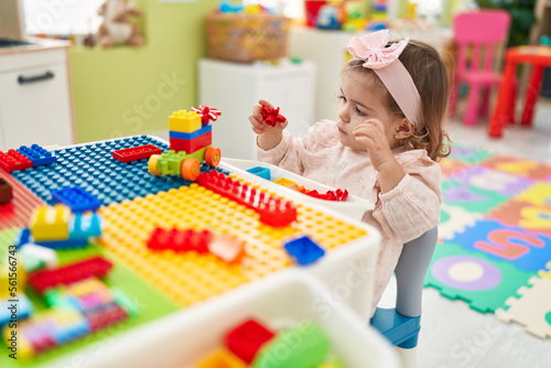 Adorable blonde toddler playing with construction blocks sitting on table at kindergarten
