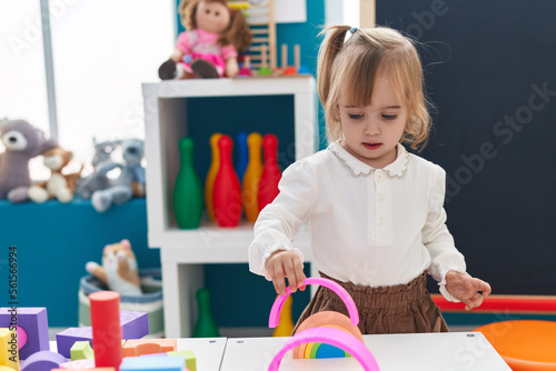 Adorable blonde girl playing with toys standing at kindergarten