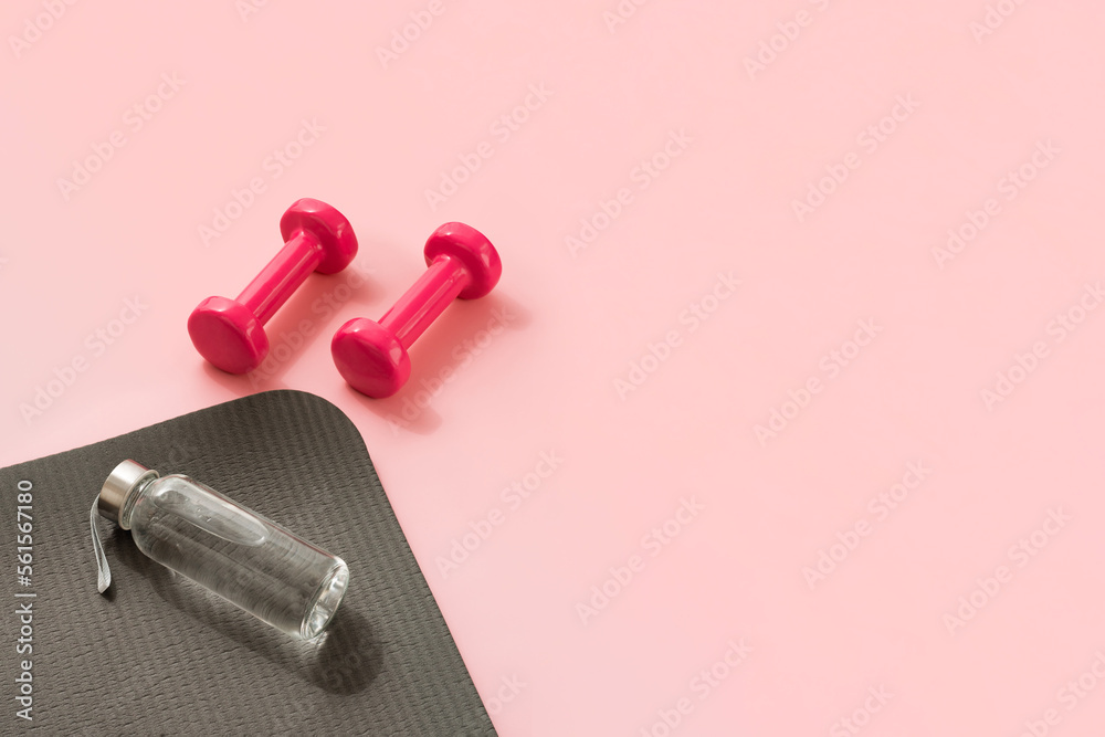Stylish gray and pink fitness training and gym concept. Perspective view of gray sport mat, water bottle and pink dumbbells on pink background. Set for pilates, fitness with copy space Stylish gray and pink fitness training and gym concept. Perspective view of gray sport mat, water bottle and pink dumbbells on pink background. Set for pilates, fitness with copy space