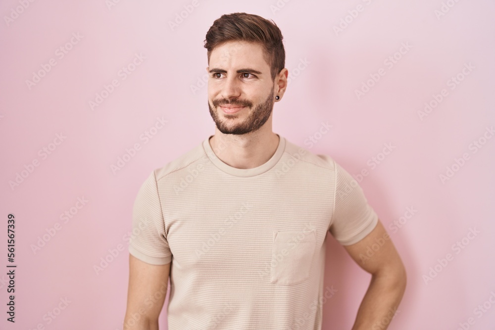 Hispanic man with beard standing over pink background smiling looking to the side and staring away thinking.
