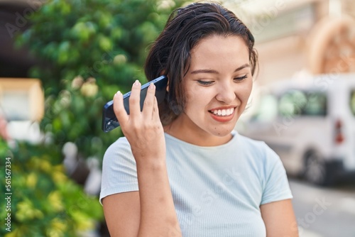 Young hispanic woman smiling confident listening audio message by the smartphone at street