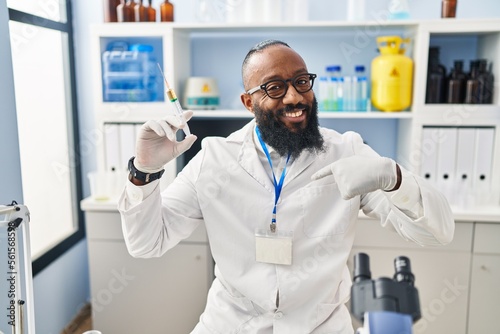 African american man working at scientist laboratory holding syringe pointing finger to one self smiling happy and proud