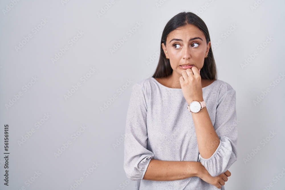 Young hispanic woman standing over white background looking stressed and nervous with hands on mouth biting nails. anxiety problem. Young hispanic woman standing over white background looking stressed and nervous with hands on mouth biting nails. anxiety problem.
