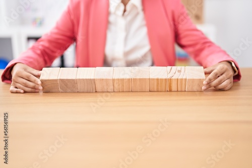 Young beautiful hispanic woman business worker sitting on table with wooden cubes at office