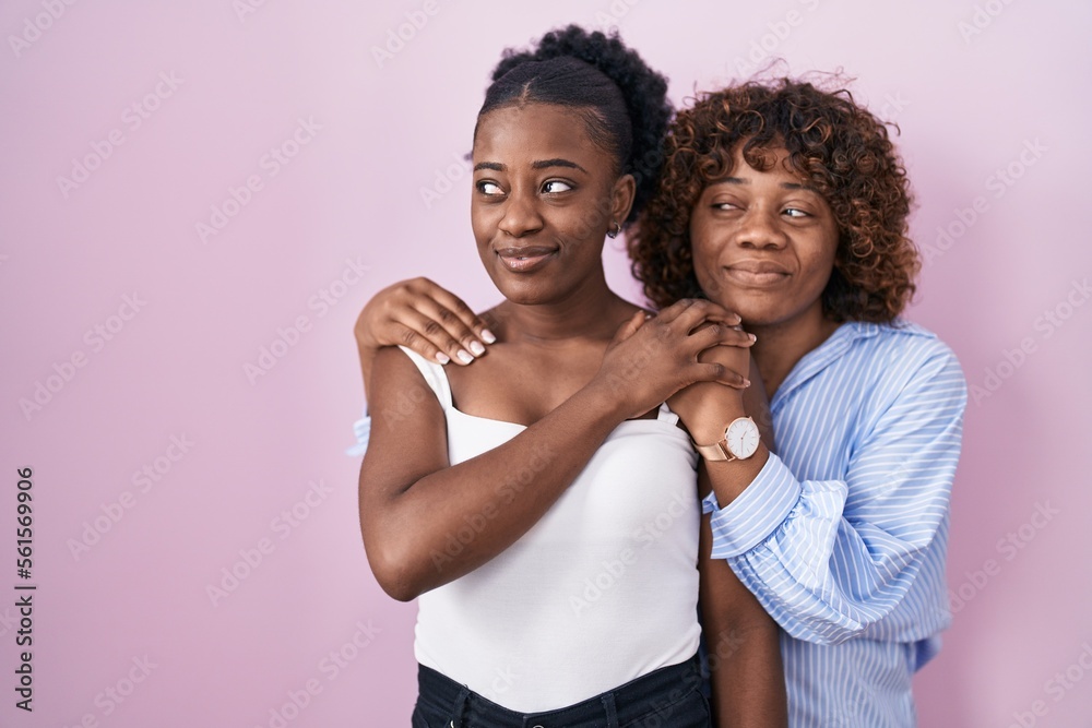 Obraz premium Two african women standing over pink background smiling looking to the side and staring away thinking.
