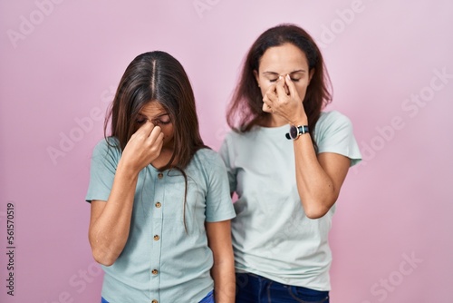 Young mother and daughter standing over pink background tired rubbing nose and eyes feeling fatigue and headache. stress and frustration concept.