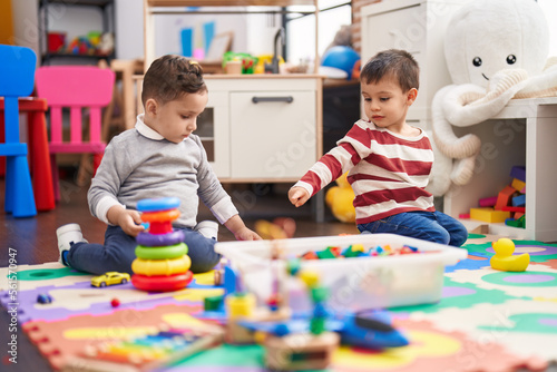 Two kids playing with toys sitting on floor at kindergarten