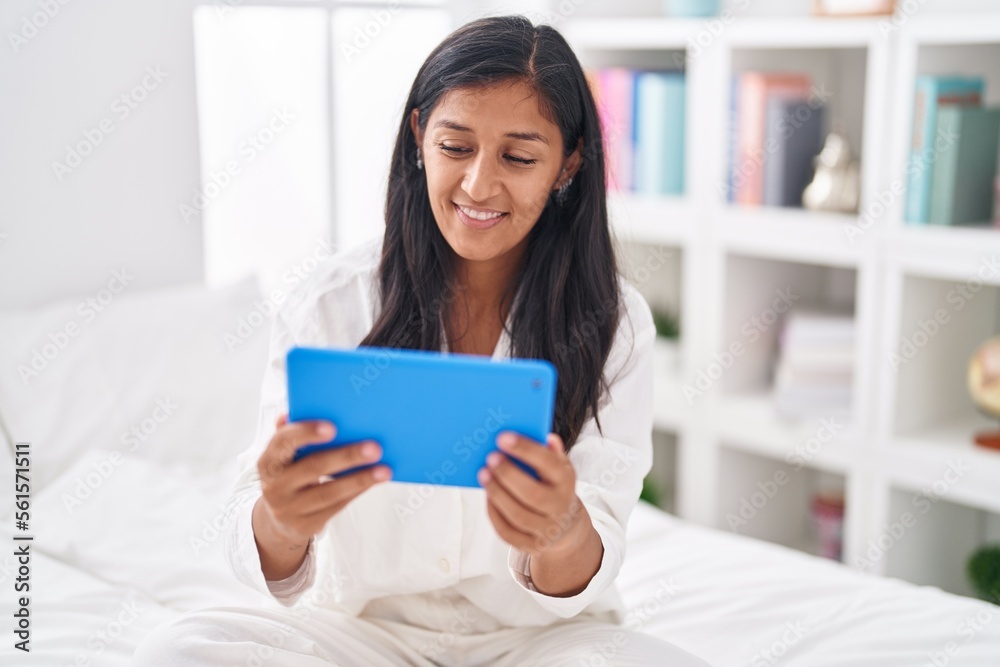 Young beautiful hispanic woman using touchpad sitting on bed at bedroom Young beautiful hispanic woman using touchpad sitting on bed at bedroom