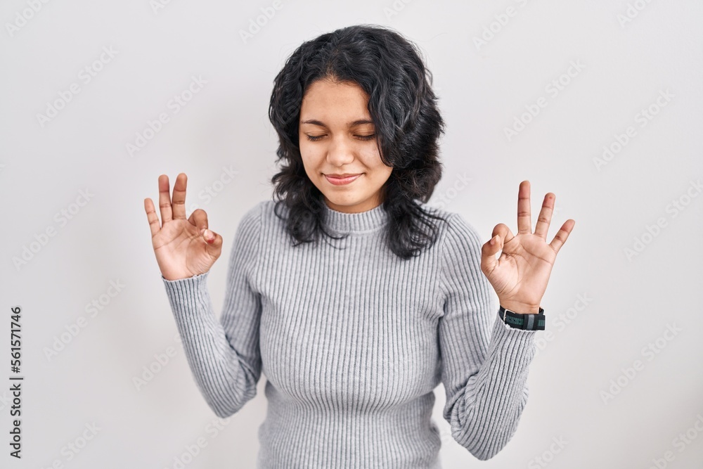 Hispanic woman with dark hair standing over isolated background relaxed and smiling with eyes closed doing meditation gesture with fingers. yoga concept.