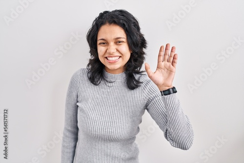 Hispanic woman with dark hair standing over isolated background waiving saying hello happy and smiling, friendly welcome gesture © Krakenimages.com