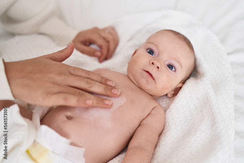 Adorable caucasian baby lying on bed applying cream on body skin at bedroom Adorable caucasian baby lying on bed applying cream on body skin at bedroom