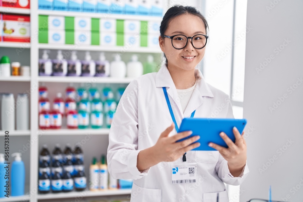 Young chinese woman pharmacist using touchpad working at pharmacy