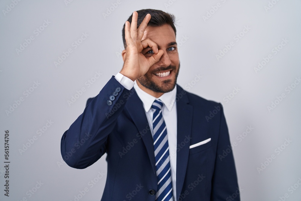 Handsome hispanic man wearing suit and tie doing ok gesture with hand smiling, eye looking through fingers with happy face. Handsome hispanic man wearing suit and tie doing ok gesture with hand smiling, eye looking through fingers with happy face.