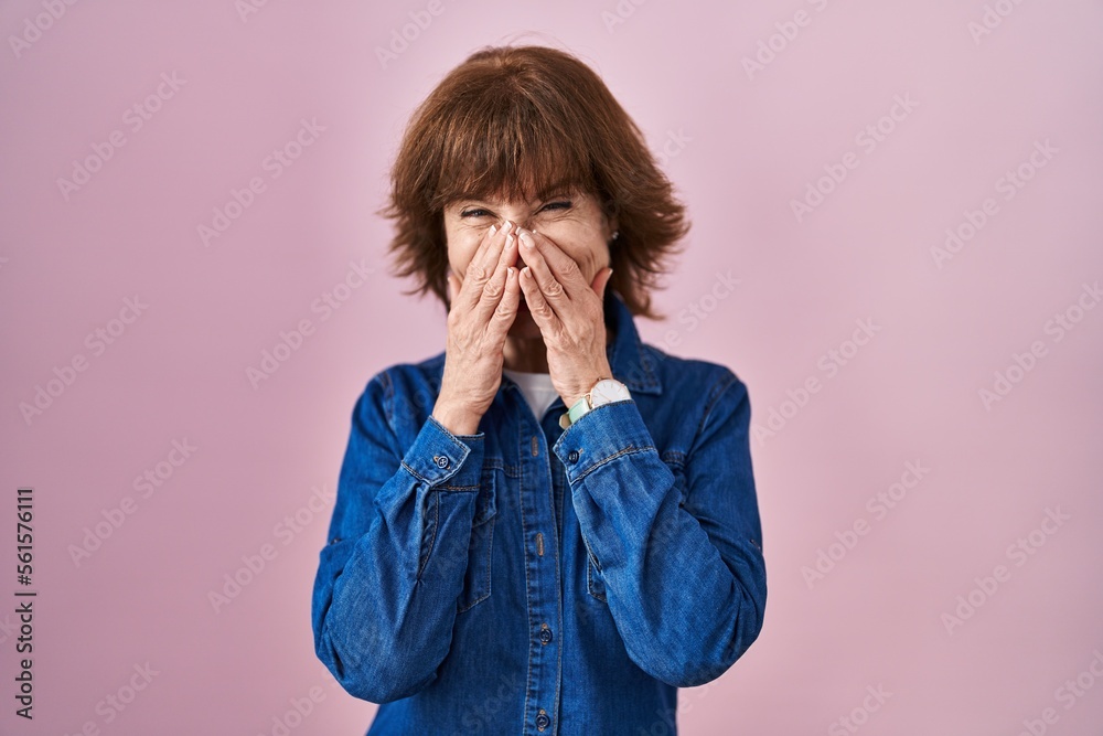 Middle age woman standing over pink background laughing and embarrassed giggle covering mouth with hands, gossip and scandal concept Middle age woman standing over pink background laughing and embarrassed giggle covering mouth with hands, gossip and scandal concept