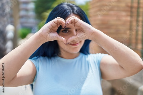 Young caucasian woman smiling confident doing heart gesture with hands over eye at street