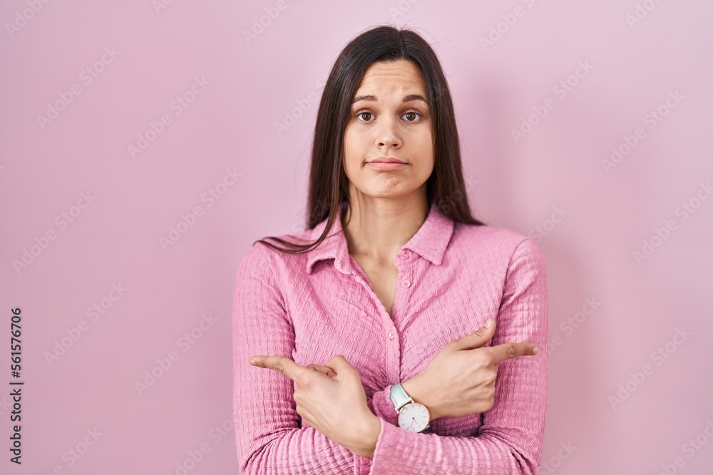 Fototapeta premium Young hispanic woman standing over pink background pointing to both sides with fingers, different direction disagree