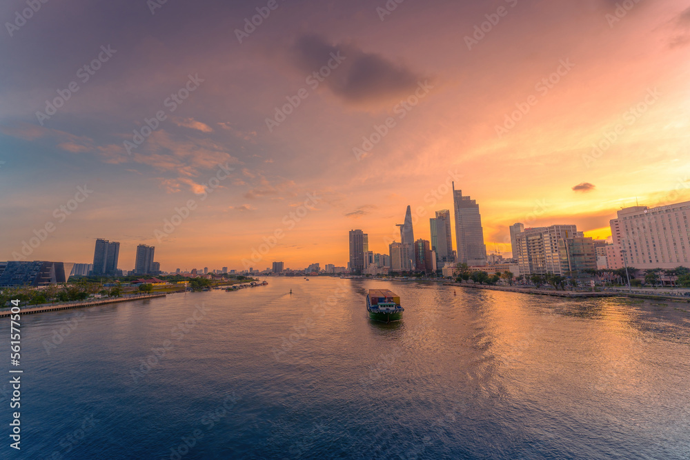 Aerial sunset view of Bitexco Tower, buildings, roads, Bason bridge and Saigon river in Ho Chi Minh city, container cargo ship on Saigon river. Travel concept.
