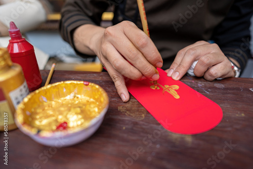 Selective focus of hand of Vietnamese scholar writes calligraphy at lunar new year. Calligraphy festival is a popular tradition during Tet holiday. Text in photo mean Happy New Year and Peace. photo