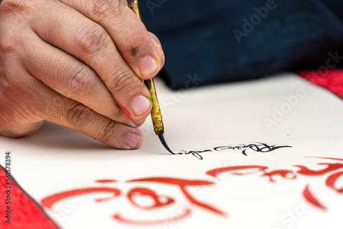 Selective focus of hand of Vietnamese scholar writes calligraphy at lunar new year. Calligraphy festival is a popular tradition during Tet holiday. Text in photo mean Happy New Year and Peace. photo