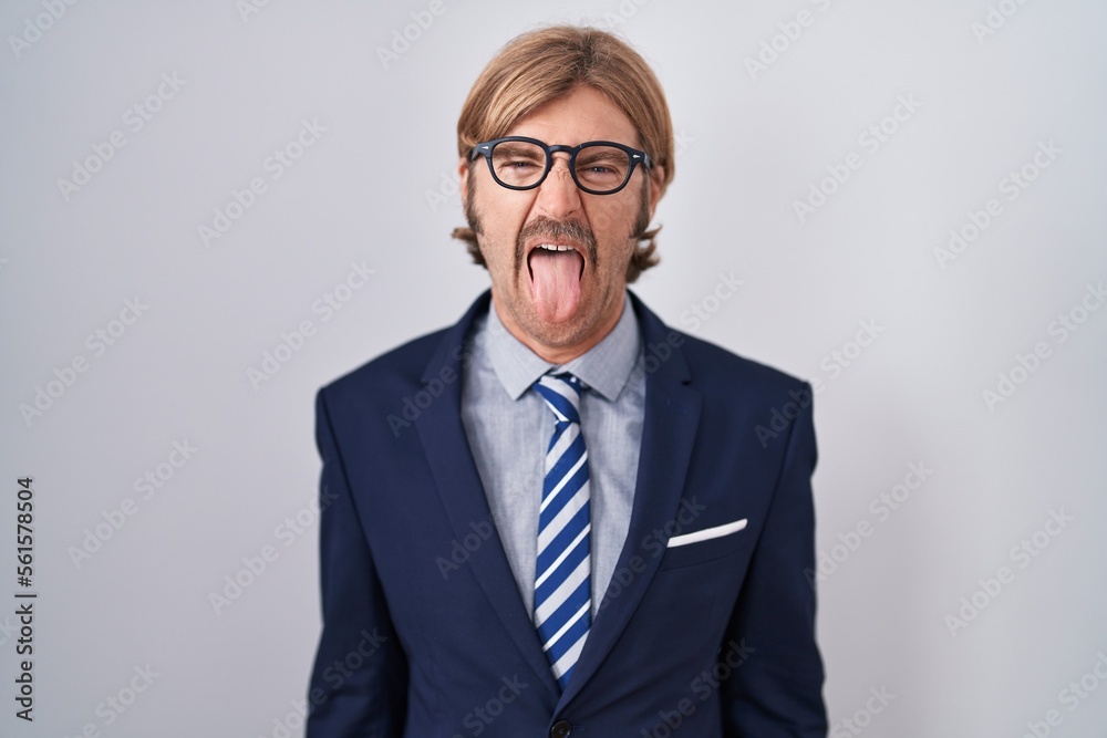 Caucasian man with mustache wearing business clothes sticking tongue out happy with funny expression. emotion concept.