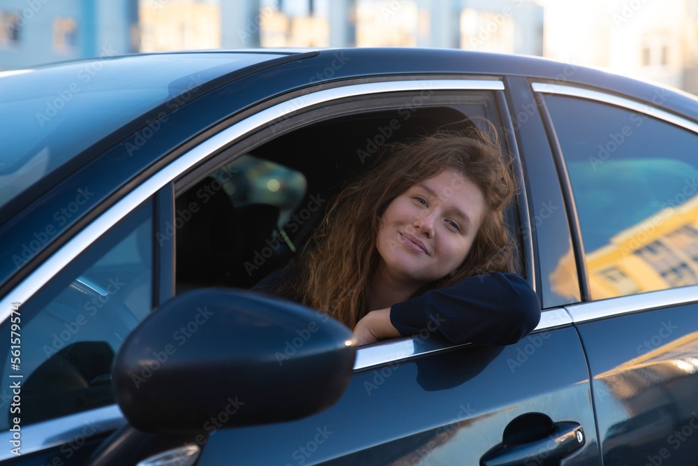 Portrait of happy positive girl, young woman driver is sitting in her car, new automobile, enjoying driving, having fun, laugh. Joyful lady in auto looking at camera