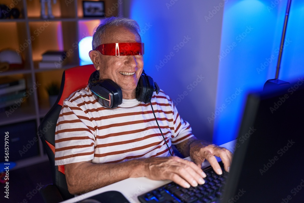 Middle age grey-haired man streamer playing video game using virtual reality glasses at gaming room