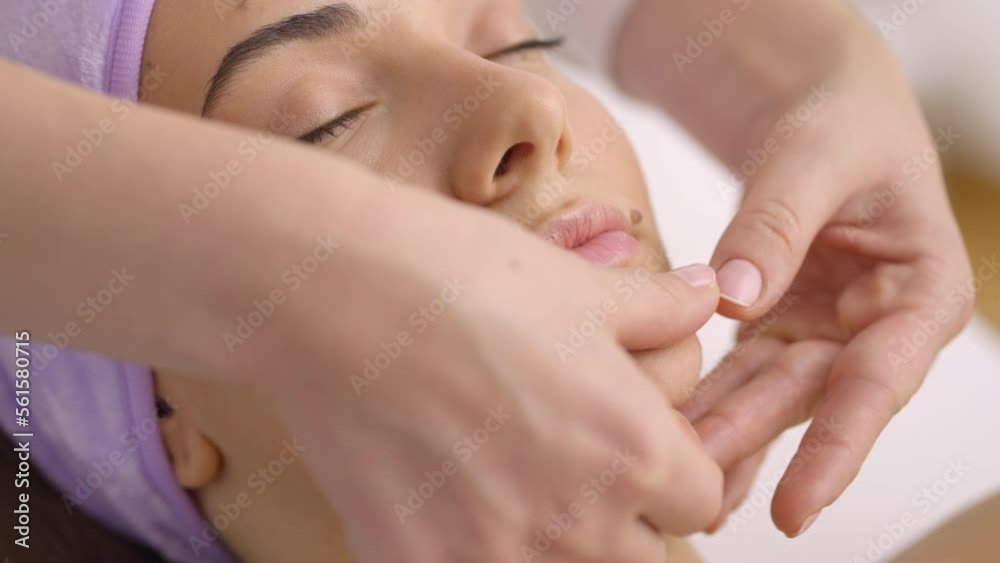 Beautiful young woman receiving facial massage at beauty spa. Woman having facial treatment in slow-motion Beautiful young woman receiving facial massage at beauty spa. Woman having facial treatment in slow-motion