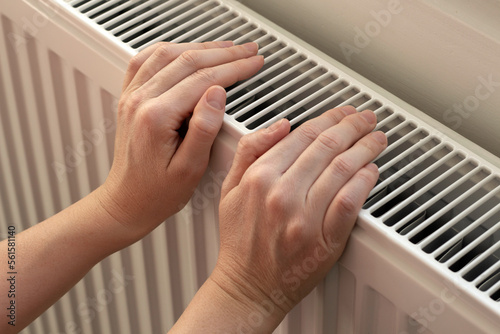 A woman warms hands on a radiator. Home heating. Low temperature and cold in the house. Photo closeup