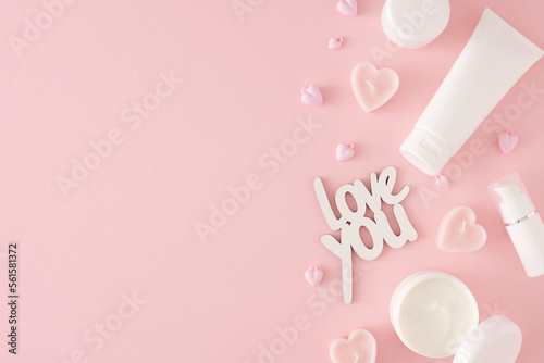 Women day concept. Top view photo of cosmetic bottles, cream jars, heart shaped candles and inscription love you on pastel pink background with copy space. Mother's day Or Valentines idea.
