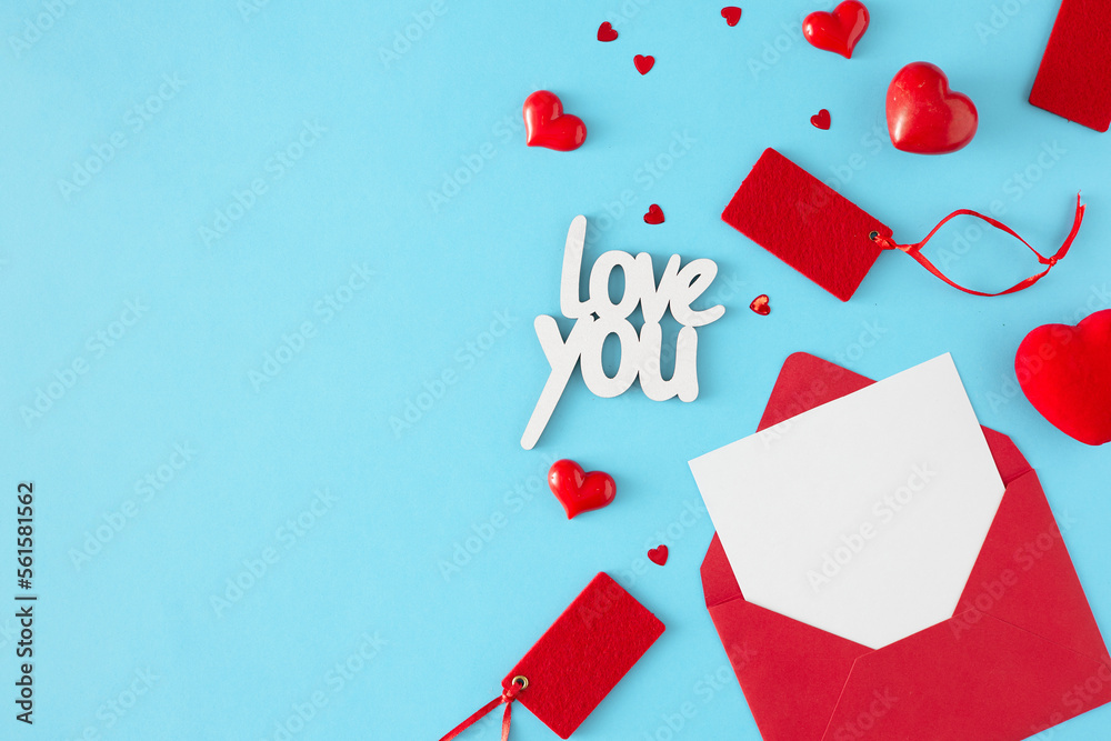 Mothers or women day concept. Top view photo of open red envelope with white card, red hearts, sale tags and inscription love you on pastel blue background with copy space. Mothers or women day concept. Top view photo of open red envelope with white card, red hearts, sale tags and inscription love you on pastel blue background with copy space.