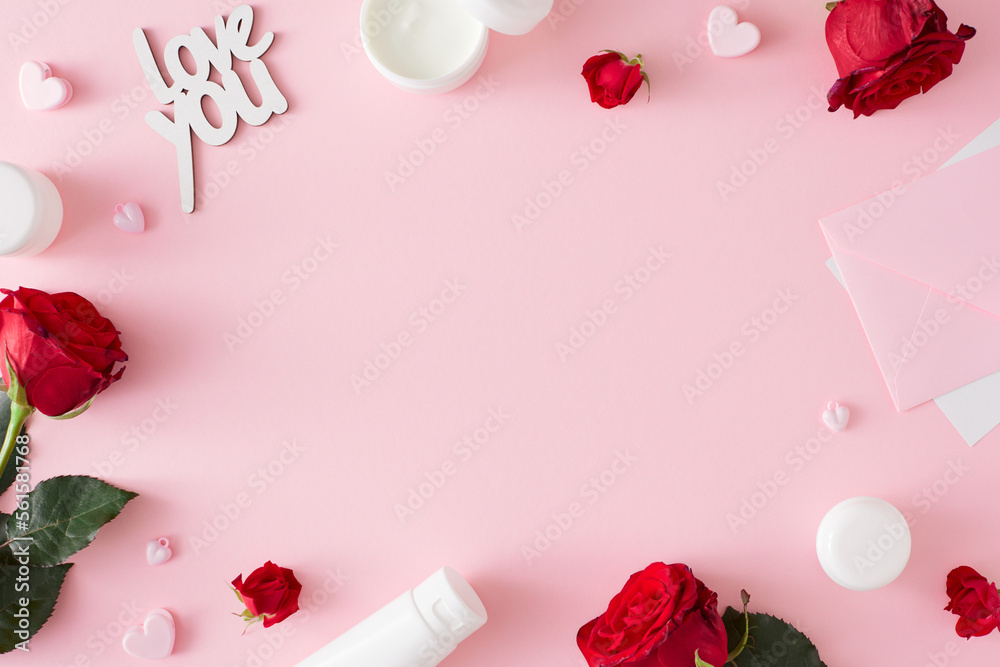 Mother's day concept. Top view photo of cosmetic bottles, red roses, envelope and inscription love you on pastel pink background with copy space in the middle. Holiday card idea.