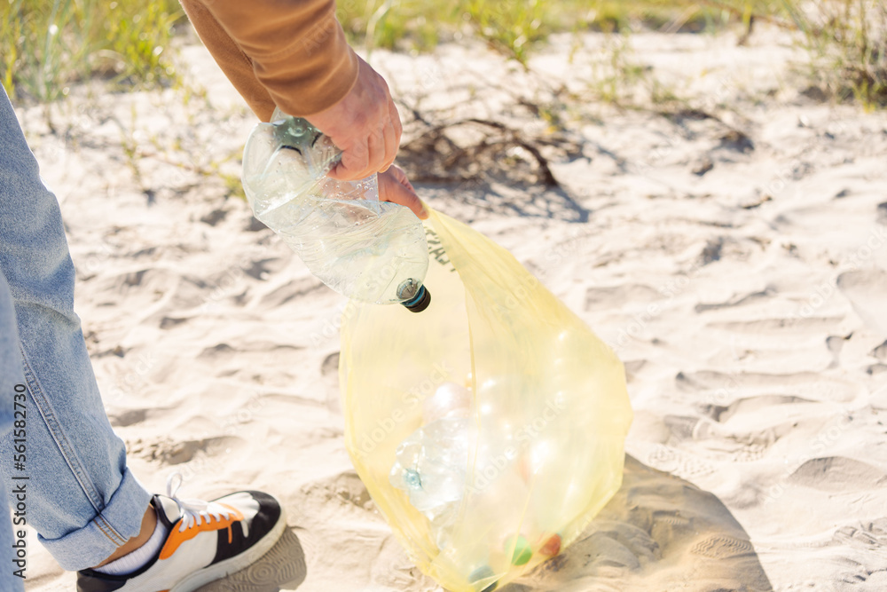 Obraz premium Trash on the beach. Men hand collects bottle plastic on sea beach. World environment day concept.