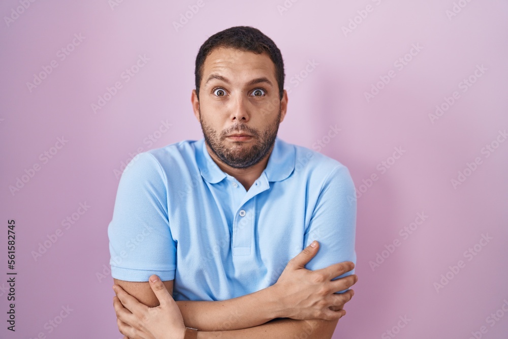 Hispanic man standing over pink background shaking and freezing for winter cold with sad and shock expression on face