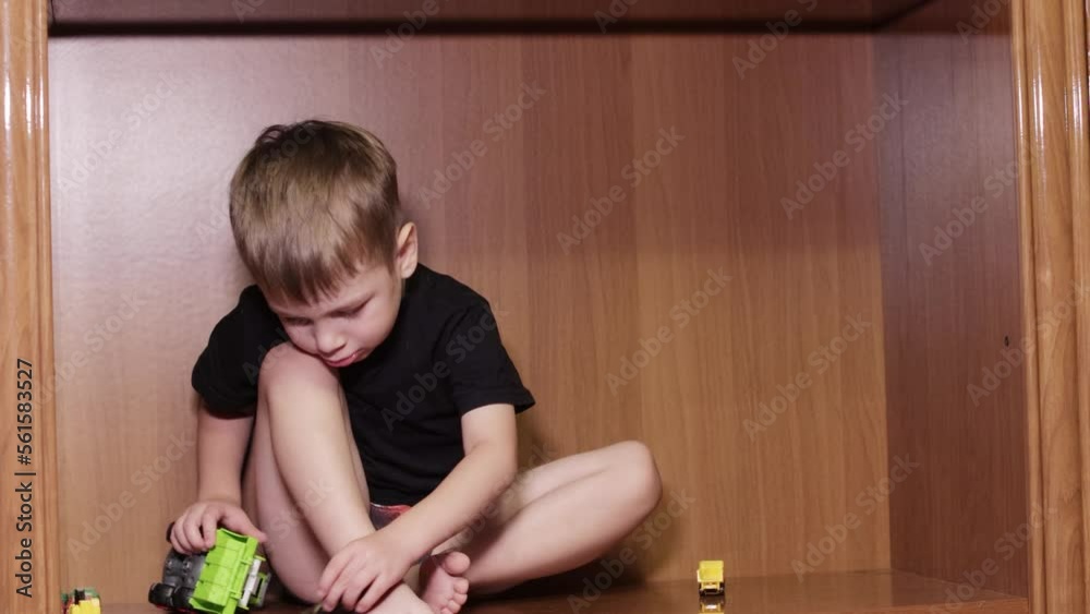 The boy plays with cars sitting in closet