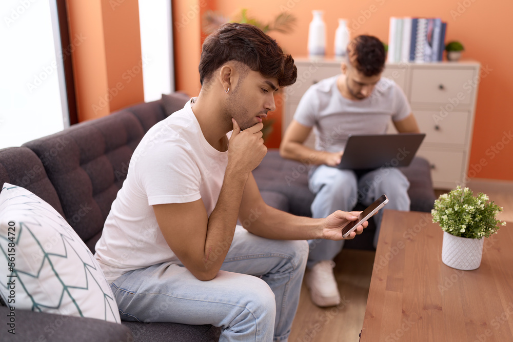 Two hispanic men couple using laptop and smartphone sitting on sofa at home Two hispanic men couple using laptop and smartphone sitting on sofa at home