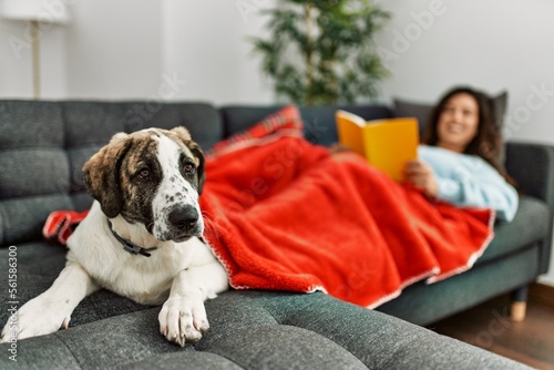Young woman reading book lying on sofa with dog at home