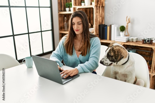 Young woman using laptop sitting on table with dog at home