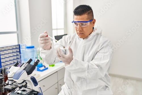Fototapeta Naklejka Na Ścianę i Meble -  Young latin man scientist pouring liquid on cannabis herb sample at laboratory
