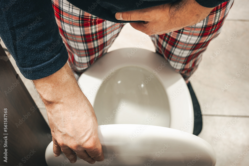 Urination problem, A man in pajamas in the toilet squeezes his crotch and lifts the toilet seat, Health concept, Male prostate problem, urinary system function, bladder pain
