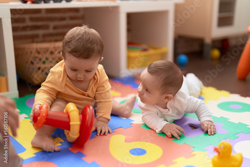 Two toddlers playing with toys sitting on floor at kindergarten