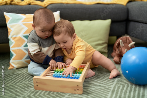 Two toddlers playing with abacus sitting on floor at home